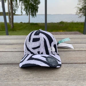 Zebramönstrad keps från The North Face - Snygg keps från The North Face med svartvitt zebramönster och justerbar snapback baktill. Framsidan har broderad logga och materialet är lätt och ventilerande polyester, perfekt för soliga dagar.