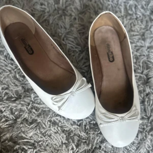  ballerinaskor - Snygga vita ballerinaskor från Din Sko med rund tå och söt rosettdetalj framtill. Skorna har en klassisk och stilren design som passar perfekt till både jeans och klänning. Tillverkade i syntetmaterial med mjuk innersula för extra komfort. Postar samma dag som du köper innan 20/21.00