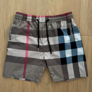 Burberry shorts  - Säljer dessa sköna burberry shorts, aldrig använda. Shortsen har elastisk midja med svart snörning och en bakficka. Perfekta för stranden eller poolen.