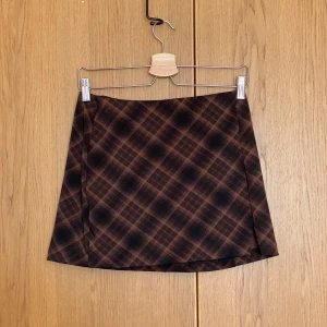 Brun rutig minikjol  - Brun och svart rutig minikjol från H&M. Kjolen har en liten slits framtill och är i stretchigt material. Bara använd en gång 