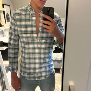Rutig skjorta från Ralph Lauren S - Säljer en klassisk rutig skjorta från Ralph Lauren i grönt, blått och vitt. Skjortan har button-down krage, lång ärm och den ikoniska rosa loggan broderad på bröstet. Perfekt för dig som gillar en stilren och tidlös look.