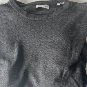 Mörkgrå stickad tröja Jack & Jones - En stilren mörkgrå stickad tröja från Jack & Jones i storlek S, passar även M. Tröjan har rund halsringning och är perfekt för lager-på-lager. Enkel design som funkar till många olika outfits. 