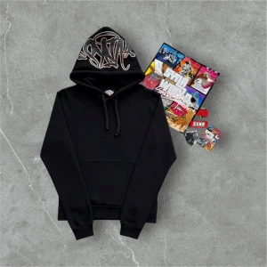 Syna World - Black & Gold Limited Edition steeetwear - Svart hoodie från Syna med stort grafitti-inspirerat tryck på huvan i beige/rosa toner. Tröjan har klassisk känguruficka, breda snören och mjukt material på insidan. Perfekt för dig som gillar streetwear och vill sticka ut med coola detaljer.