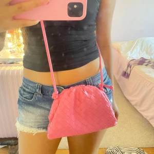 Rosa axelväska i flätad skinnimitation - Säljer en superfin rosa flätad väska med en lång och justerbar axelrem. Går att ta bort bandet helt om man vill göra det till en clutch.  Kommer inte ihåg vart jag köpte den men säljer då jag inte har fått mycket användning för den. 