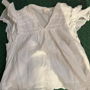 Vit blus med volangärmar - Säljer en luftig vit blus från Gina Young med v-ringning och fina volangärmar. Blusen har broderade detaljer upptill. Perfekt för varma dagar eller när du vill ha en romantisk look.