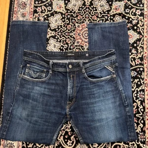 Replay Anbass 32/30 Mörkblå - Säljer ett par klassiska blå jeans från Replay med snygg tvätt och raka ben. Jeansen har fem fickor, kontrastsömmar och läderpatch bak i midjan. Perfekta för dig som gillar en tidlös och avslappnad stil.