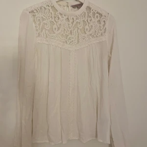 Vit spetsblus från KappAhl - Supersöt vit blus från KappAhl med långärmade ärmar och vackra spetsdetaljer upptill. Blusen har hög halsringning och dekorativa spetsband framtill. 