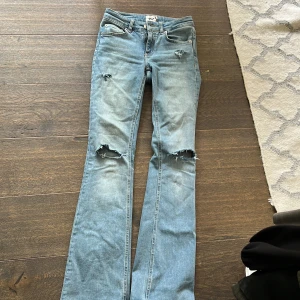 Ljusblå bootcut jeans med slitningar - Säljer ett par ljusblå jeans med bootcut passform och snygga slitningar på knäna och låret. Jeansen har klassisk femficksdesign, normal midja och är tillverkade i mjukt denimtyg. Jag säljer dom för att aldrig kommer till användning men dom är i nyskick! 