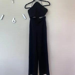 Svart byxdress från Gina Tricot XS - Snygg svart byxdress från Gina Tricot med smala axelband och cut out-detaljer i midjan. Vida ben och dragkedja i ryggen. Använd fåtal gånger.