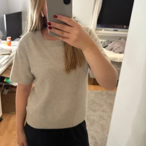 Beige stickad kortärmad tröja H&M - Beige stickad tröja från H&M med korta ärmar och rund halsringning. Tröjan har en enkel och clean look med ribbade kanter vid hals, ärmslut och nederkant. Perfekt för lager-på-lager och chill vardagsstil.