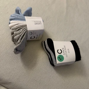 5-pack bomullsstrumpor från C - Två 5-pack strumpor från C i olika färger. Ena paketet innehåller ljusblå, grå och vita strumpor, det andra svart, grå och vita. Alla är i mjuk bomullsmix och har enkel, klassisk design. Perfekta för dig som gillar stilrena och bekväma strumpor till vardags.