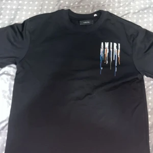 Svart Amiri t-shirt med färgstänk - Svart t-shirt från Amiri med coolt tryck av droppande färg och stor logga både fram och bak. T-shirten har rund hals, korta ärmar och är gjord i mjuk bomull. Perfekt för dig som vill sticka ut med streetstyle-vibe.