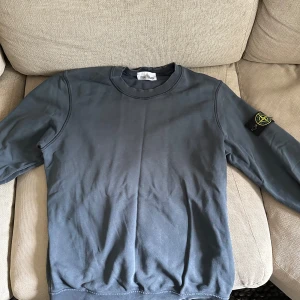 Mörkgrå Stone Island sweatshirt - Säljer en mörkgrå crewneck från Stone Island med klassisk rund hals och ikonisk patch på vänster ärm. Tröjan är i mjuk bomull och har långa ärmar. Finns en liten skada på tröjan men syns knappt inte vid användning. Köpt på NK. Äkta. Nypris 2500kr