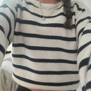 Randig stickad tröja i vitt och svart - Mysig stickad tröja med breda svarta ränder på vit botten. Tröjan har en klassisk rund halsringning och långa ärmar. Den är lite croppad och har en relaxed fit, perfekt för en chill och stilren look.