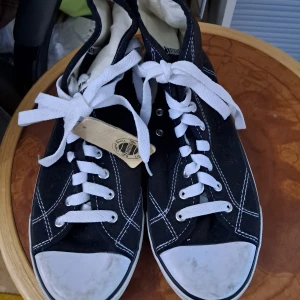 Svarta sneakers från Donnay - Klassiska svarta sneakers från Donnay med vita kontrastsömmar och vita snören. Skorna har rund tå, platt sula i gummi och är tillverkade i canvas. Snygg retrostil med logga på sidan och tåhätta i vitt. Perfekta för en avslappnad streetlook. De är lite smutsiga (går säkert att torka bort) och aldrig använda :)