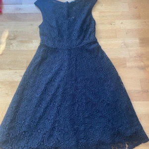 Svart spetsklänning från STOCKH LM - Säljer en svart klänning från STOCKH LM i storlek 38. Klänningen har vackert spetsmaterial med blommigt mönster, är ärmlös och har en klassisk, något utställd siluett som slutar strax under knäna. Perfekt för dig som gillar eleganta detaljer.