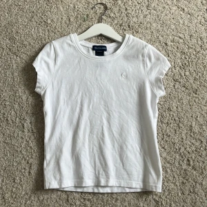 Vit t-shirt från Ralph Lauren - Klassisk vit t-shirt från Ralph Lauren med rund hals och korta ärmar. Tillverkad i mjuk bomull med lite stretch för extra komfort. Diskret broderad logga på bröstet. Perfekt basic-plagg att matcha med allt. Den är väldigt liten i storlek🩷🩷