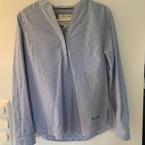 Blåprickig henley från Bondelid - Snygg blå henley-skjorta från Bondelid med tunna vita ränder och små svarta prickar. Skjortan har lång ärm, v-ringad hals och broderad Bondelid-logga nedtill. Tillverkad i mjuk bomull, perfekt för en chill och stilren look. Jättefint skick! Skriv om ni har frågor eller vill ha mer bilder🤗