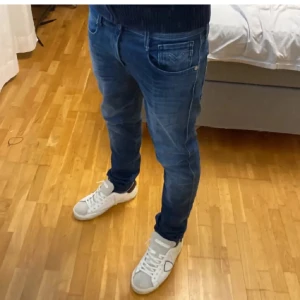Blå Replay jeans slim fit - Säljer ett par snygga blå Replay jeans med slim passform. Jeansen har klassisk femficksdesign, diskreta slitningar och tydliga sömmar. Modellen är smal och sitter tajt längs benen. Perfekta för dig som gillar en modern och stilren look. Storlek 30/34