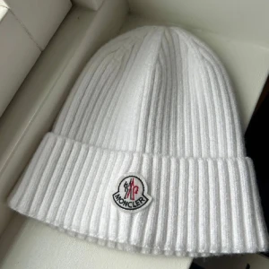 Vit ribbstickad mössa från Moncler - Snygg vit ribbstickad mössa från Moncler med klassisk uppvikt kant och broderad logotyp framtill. Tillverkad i mjukt material som håller dig varm och ger en clean look. Perfekt accessoar för kyliga dagar och enkel att matcha med olika outfits.
