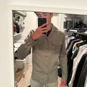 Grön overshirt från Bondelid - Säljer en stilren overshirt från Bondelid. Jackan har klassisk krage, två bröstfickor med lock och knappar framtill. Tillverkad i ett skönt linnematerial som passar perfekt till lager-på-lager. Enkel att matcha med jeans eller chinos. Använd endast fåtal gånger. Bara att höra av sig vid frågor!