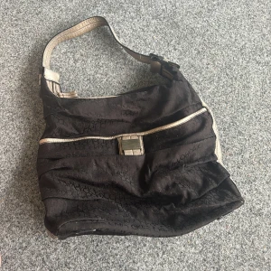 Svart axelväska från Calvin Klein - Svart axelväska från Calvin Klein med diskret CK-monogram över hela väskan. Väskan har metallicfärgade detaljer och axelrem i syntetmaterial. Snyggt spänne framtill och mjuk, lite slouchy form. Perfekt för dig som gillar stilrena accessoarer med en twist. Vintage❤️