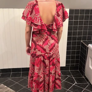 Johanna Ortis X H&M NY MED PRISLAPP! Blommig långklänning med volang - Säljer en superfin långklänning med blommigt mönster i rött och beige. Klänningen har v-ringning, volangdetaljer över axlarna och en öppen rygg. Materialet känns lätt och luftigt, perfekt för varma dagar. Passformen är normal och klänningen har korta ärmar.