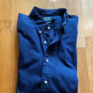  Ralph Lauren skjorta - Snygg marinblå skjorta från Polo Ralph Lauren i custom fit. Skjortan har klassisk krage, knäppning framtill och den ikoniska broderade loggan på bröstet. Hör av dig vid funderingar! Mvh Carl