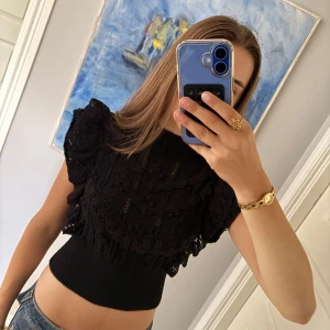 Festtopp från Zara - Supersnygg svart topp med fina detaljer och volang på axlarna. Croppad modell med ribbad midja och hög hals. Perfekt för dig som vill ha en trendig och unik topp med mycket detaljer.