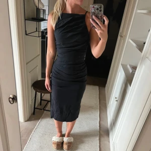 Tight svartklänning från Zara  - Snygg svart långklänning med smala axelband och figurnära passform. Klänningen har draperade detaljer framtill och en liten slits bak. Perfekt för dig som gillar stilrena och eleganta plagg med en modern touch.