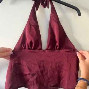 Vinröd halterneck festtopp - Helt oanvänd vinröd festtopp från Gina tricot! Glansigt material med en djup v-ringning och öppen rygg! Toppen knyts i nacken och på ryggen för en justerbar passform. Sjukt snygg men har tyvärr aldrig fått tillfälle att använda den. Populär modell som inte längre säljs. Prislapp kvar, endast provad! Perfekt för fest❤️ nypris: 360kr