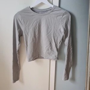 Ljusgrå croppad långärmad topp 157 - En stilren ljusgrå croppad långärmad topp från 157. Tillverkad i mjuk bomullsmix med enkel rund halsringning. Perfekt att matcha med jeans eller kjol för en clean look.