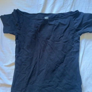 Svart offshoulder topp från 157 - En svart offshoulder topp från 157 i mjuk bomullsblandning med stretch. Toppen har korta ärmar och en tight passform som sitter snyggt över axlarna. Perfekt för dig som gillar en enkel men stilren look.