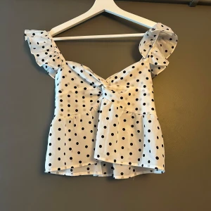 Prickig volangtopp från Romwe - Supersöt vit topp från Romwe med svarta prickar och volangiga axelband. Skicket är bra! Säljer denna då axelbanden är för stora på mig ! Super söt och fin annars❤️