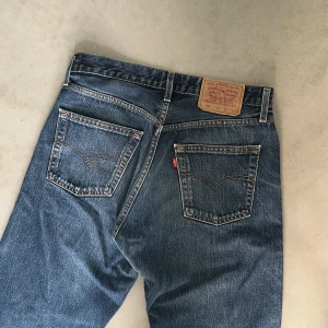 Levi's 590  - Klassiska Levi's 590 jeans i mörkblå denim med raka ben och femficksmodell. Jeansen har den ikoniska läderpatchen bak i midjan och synliga nitar. Perfekta för dig som gillar en tidlös och avslappnad look.