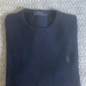 Mörkblå stickad tröja Polo Ralph Lauren - Snygg mörkblå stickad tröja från Polo Ralph Lauren i storlek M. Hör av er vid frågor och funderingar. Kan förhandla om pris vid snabb affär. Säljs bildligt på grund av ett litet hål nertill på tröjan 