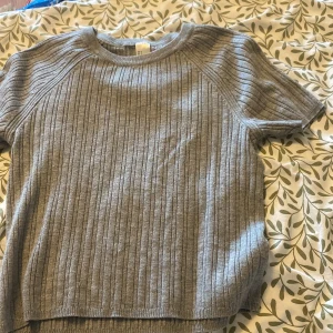 Grå figursyd stickad tröja  - Säljer en grå ribbad stickad tröja i storlek S. Tröjan har korta ärmar och rund halsringning. Perfekt för dig som gillar en enkel men stilren look. Passar bra till både jeans och kjol.