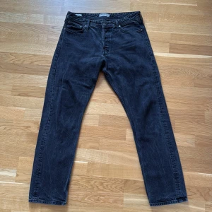 Svarta straight jeans från Jack & Jones - Säljer ett par svarta jeans från Jack & Jones med klassisk femficksdesign och raka ben. Jeansen har en mörk tvätt och är tillverkade i slitstarkt denim med normal passform. Perfekt för dig som gillar en enkel och tidlös stil.