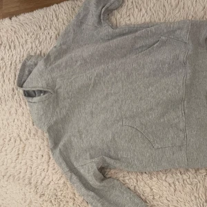 Grå hoodie från WAI WAI - Fin grå hoodie med klassisk känguruficka och huva. Perfekt för chill dagar eller när du vill ha en enkel och stilren look. Mjuk och skön bomullsblandning, långärmad och normal passform.