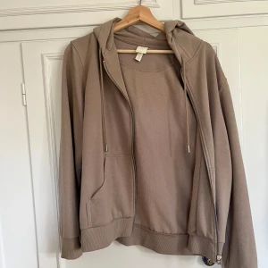 Beige hoodie från H&M med dragkedja - Säljer en beige hoodie från H&M med huva och dragkedja framtill. Tröjan har långa ärmar, ribbade muddar och fickor på sidorna. Perfekt för chill/mys dagar och enkel att matcha med jeans eller mjukisbyxor.🤎