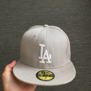 Grå LA Dodgers keps från New Era - Snygg grå LA Dodgers 59FIFTY keps från New Era med broderad LA-logga framtill och World Series-detalj på sidan. Klassisk flat brim och broderade ventilationshål. Kepsen är i bomull och har en stilren look med vita broderier.