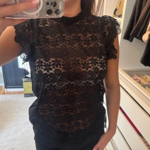 Svart spetsblus med volangärmar - Svart blus i spets med blommigt mönster och volangdetaljer på ärmarna. Genomskinlig men passar perfekt med ett tajt linne under