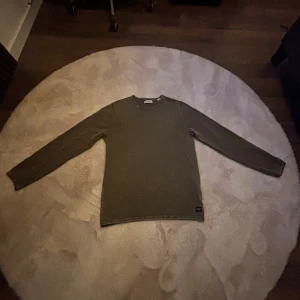 Olivgrön långärmad tröja Jack & Jones - Säljer en olivgrön långärmad tröja från Jack & Jones. Tröjan har en enkel, rund halsringning och är tillverkad i mjuk bomull. Perfekt för chill dagar och passar snyggt till jeans eller joggers. Diskret logga nertill på framsidan.