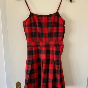 Röd rutig kortklänning från Divided - Säljer en röd och svart rutig kortklänning från Divided i storlek 34/XS. Klänningen har smala axelband och en lätt utställd kjol. Materialet är mjukt och känns som bomull, perfekt för dig som gillar en chill och snygg stil.