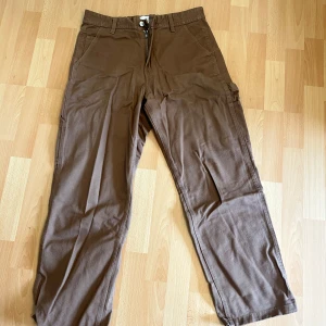 Bruna cargojeans från H&M, relaxed fit - Bruna cargobyxor från H&M i relaxed fit med raka ben och flera praktiska fickor på sidorna. Byxorna har bälteshällor, dragkedjegylf och är tillverkade i ett jeansmaterial. Perfekta för en chill och avslappnad stil.