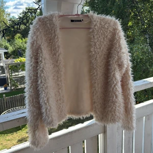 Beige pälsjacka från Gina Tricot - Supermjuk och fluffig beige pälsjacka från Gina Tricot. Jackan har lång ärm, öppen framtill och är helfodrad. Perfekt för dig som vill ha en cozy och trendig look med lite extra attityd. Passar till allt och ger en cool vibe till outfiten.