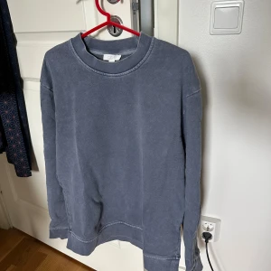 Blå sweatshirt från COS, storlek S - En blå sweatshirt från COS i storlek S. Tröjan har en klassisk rund halsringning, långa ärmar och är gjord i mjuk bomull. Färgen är dämpad blå och passformen är oversized.