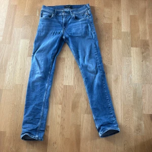Blå jeans från Replay - Säljer ett par klassiska blå jeans från Replay med snygg tvätt och raka ben. Jeansen har fem fickor, tydliga sömmar och Replay-logga på bakfickan. Perfekta för dig som gillar en tidlös och avslappnad stil. Dem är slitna med två hål ett vid gylfen och ett vid sidan av knät pris är inte hugget i sten kom med förslag👍😁
