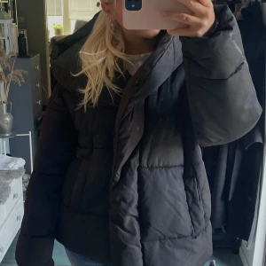 Svart pufferjacka med huva - Superfin jacka från h&m! Knapparna är trasiga och det är fläckar på den! Men jag har haft säkerhetsnål för att ha den stängd, man kan se små hål från det också! Men inget som syns så!