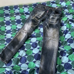 Dsquared2 blå jeans med slitningar - Säljer ett par blå jeans från Dsquared2 med coola slitningar och färgstänk. Jeansen har en skinny passform och klassisk femficksdesign. Snyggt tvättade detaljer och trasig effekt vid knät ger en edgy vibe. Perfekta för dig som gillar streetstyle. Skriv för mer bilder och kan gå ner i pris